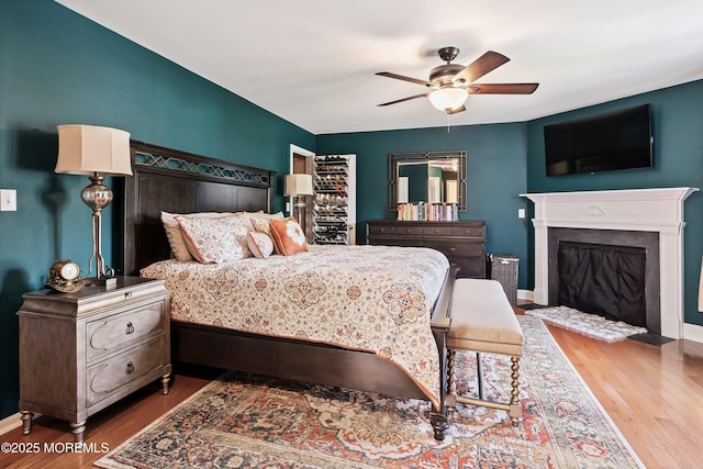 bedroom featuring a ceiling fan, a fireplace with flush hearth, baseboards, and wood finished floors