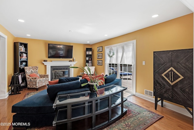 living room with a glass covered fireplace, wood finished floors, visible vents, and recessed lighting