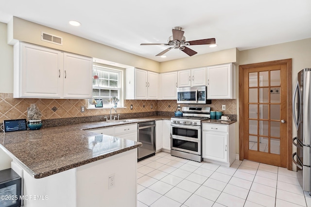 kitchen with a peninsula, visible vents, white cabinetry, appliances with stainless steel finishes, and decorative backsplash