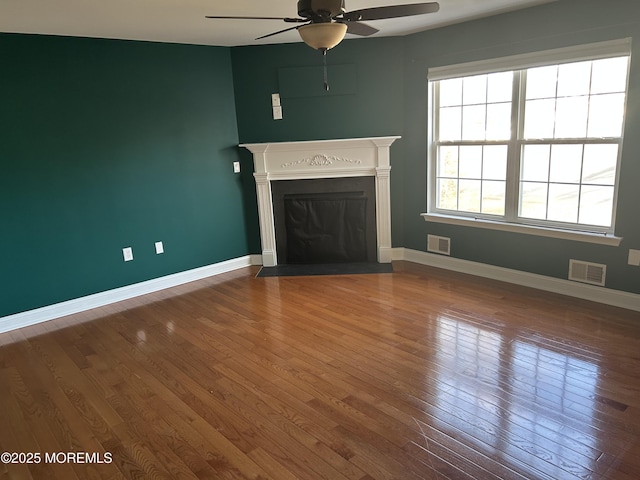 unfurnished living room featuring hardwood / wood-style flooring, a fireplace with flush hearth, visible vents, and baseboards