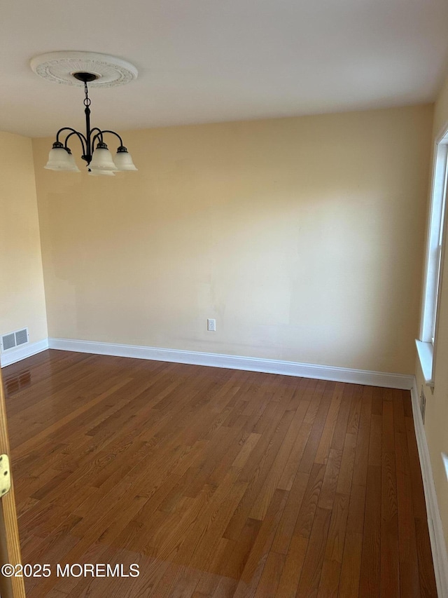 spare room with baseboards, a notable chandelier, visible vents, and dark wood-type flooring