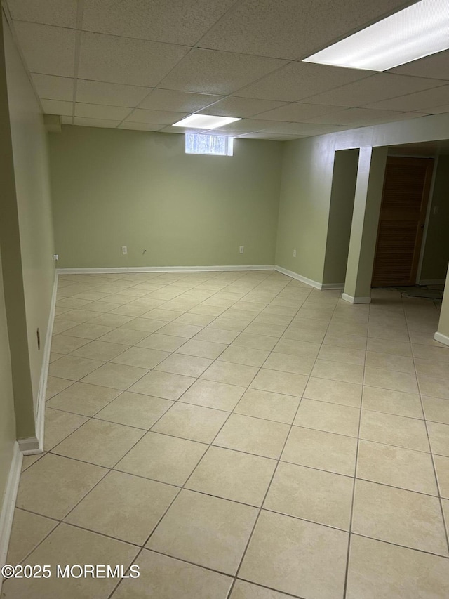 below grade area featuring a drop ceiling, baseboards, and light tile patterned flooring