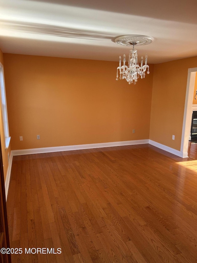 empty room featuring baseboards, a notable chandelier, and wood finished floors