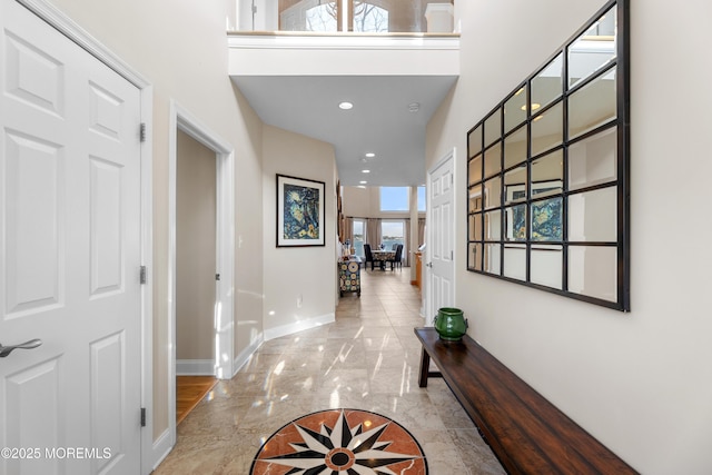 hall with recessed lighting, marble finish floor, a towering ceiling, and baseboards