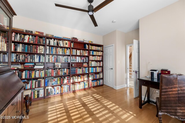 living area featuring bookshelves, baseboards, a ceiling fan, and wood finished floors