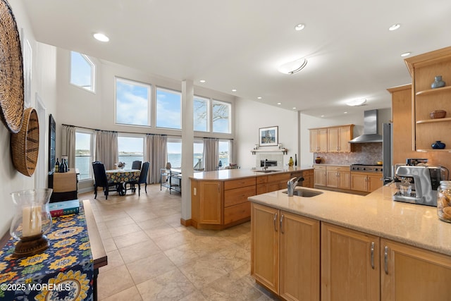 kitchen with open shelves, a sink, light stone countertops, a peninsula, and wall chimney exhaust hood