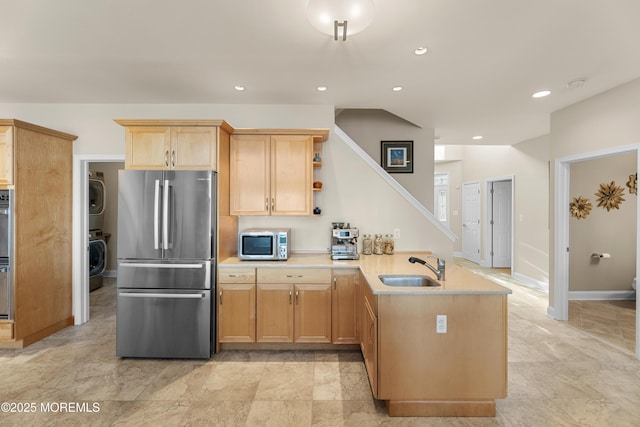 kitchen with light countertops, appliances with stainless steel finishes, a sink, stacked washing maching and dryer, and a peninsula