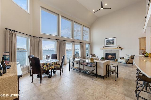 dining area featuring high vaulted ceiling, a tiled fireplace, a water view, and baseboards