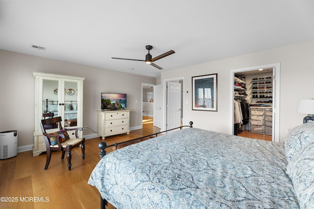 bedroom featuring a walk in closet, french doors, visible vents, wood finished floors, and baseboards