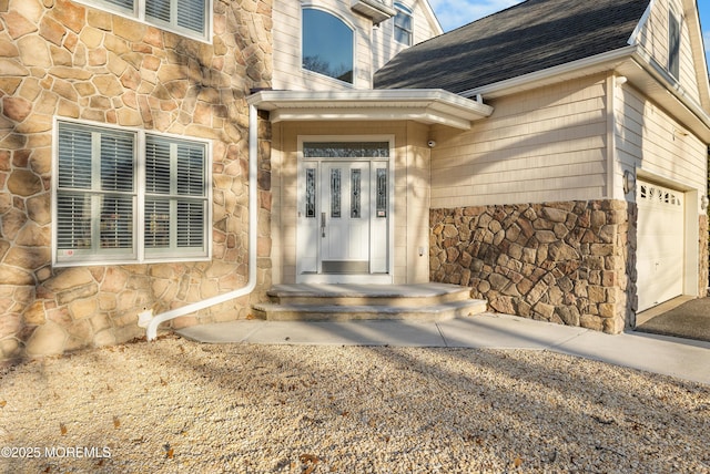 entrance to property with a garage, stone siding, and roof with shingles