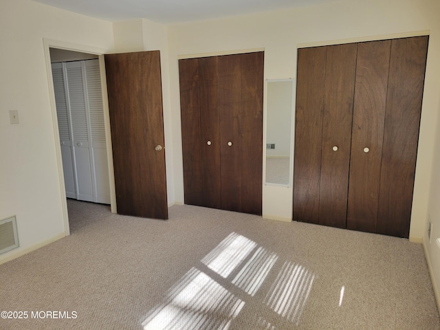 unfurnished bedroom featuring carpet flooring, two closets, and visible vents