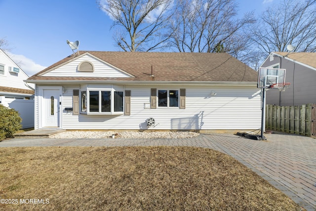 ranch-style house featuring a shingled roof and fence