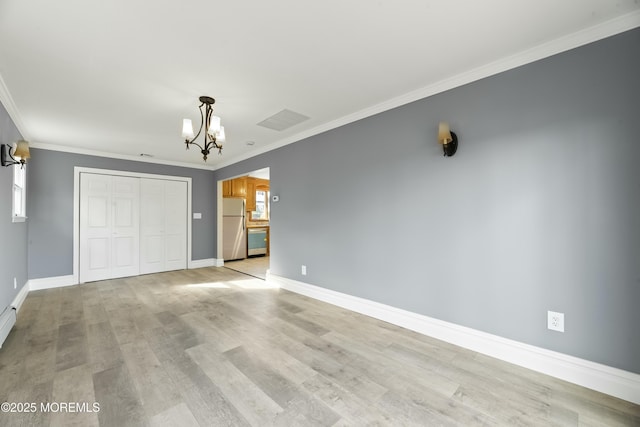 spare room featuring light wood-type flooring, baseboards, a chandelier, and crown molding