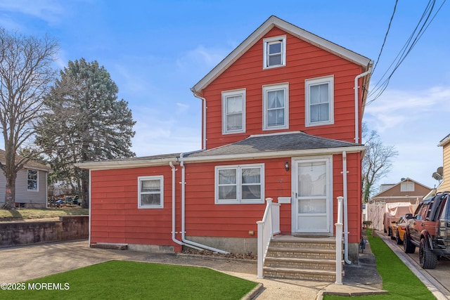 traditional home featuring entry steps, fence, a front lawn, and roof with shingles