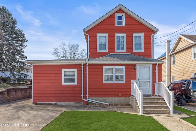 traditional-style home featuring a front lawn and roof with shingles