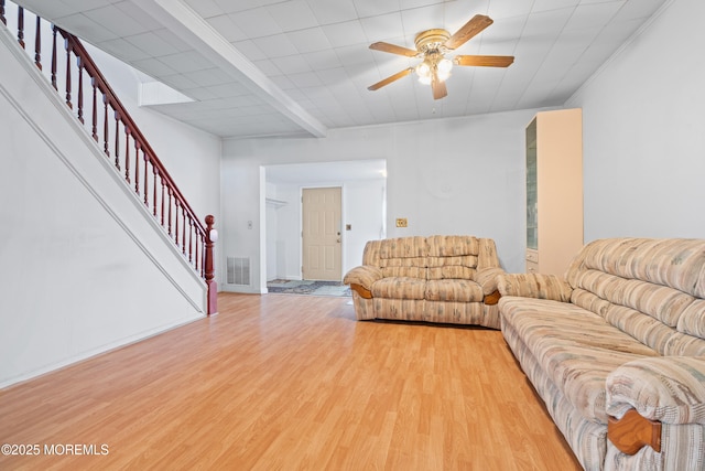 living area with light wood-type flooring, visible vents, stairway, and ceiling fan