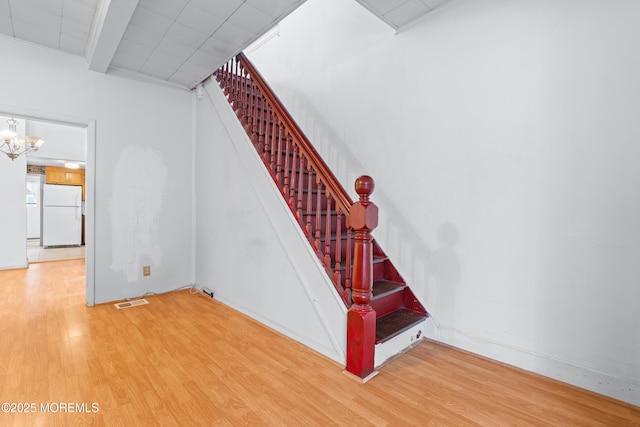 stairway with visible vents, an inviting chandelier, and wood finished floors