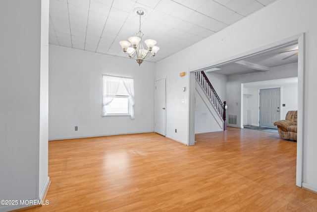 spare room featuring a notable chandelier, visible vents, light wood-style floors, stairs, and baseboards