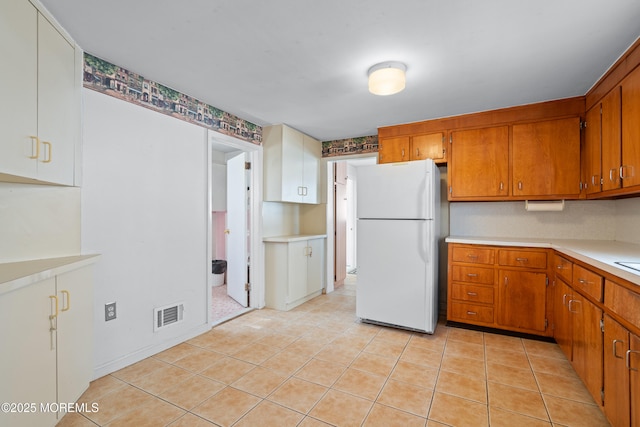 kitchen with light tile patterned floors, visible vents, light countertops, freestanding refrigerator, and brown cabinetry