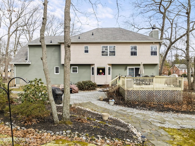 rear view of property with a deck, roof with shingles, a chimney, and a patio area