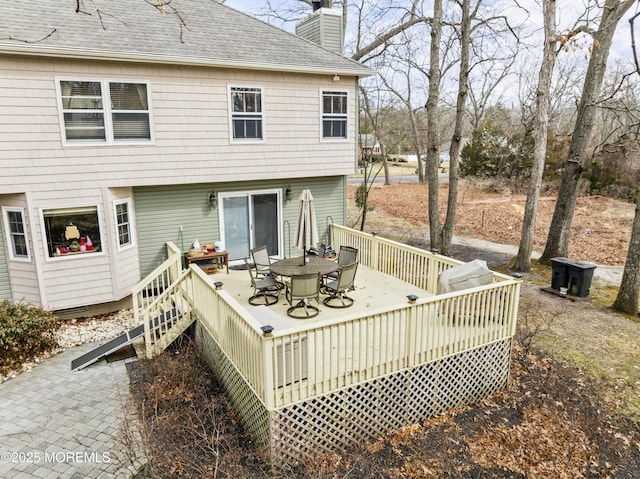 back of property featuring a deck, outdoor dining area, roof with shingles, and a chimney