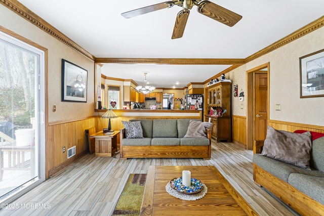 living area featuring a wainscoted wall, light wood finished floors, ornamental molding, and visible vents