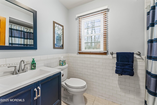 bathroom featuring toilet, a wainscoted wall, tile patterned flooring, vanity, and tile walls