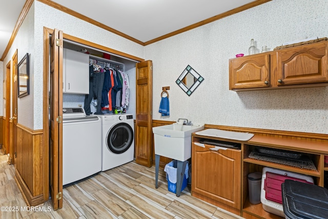 laundry room featuring cabinet space, wallpapered walls, a wainscoted wall, crown molding, and separate washer and dryer