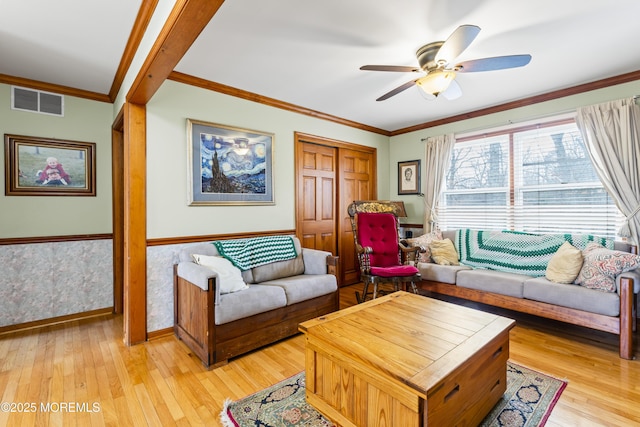 living room with light wood-style floors, wainscoting, visible vents, and ornamental molding