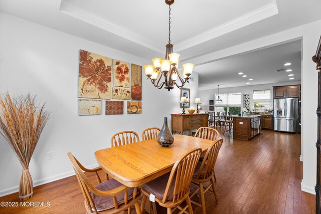 dining area with dark wood-type flooring, a tray ceiling, crown molding, and baseboards