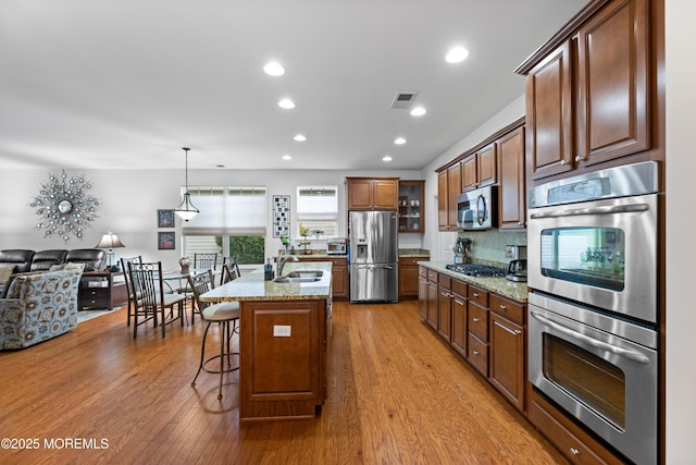 kitchen with light stone counters, appliances with stainless steel finishes, a sink, light wood-type flooring, and a kitchen bar