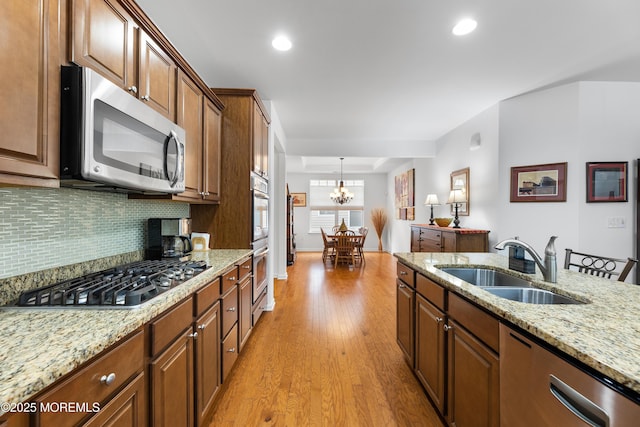 kitchen with light stone countertops, a sink, light wood-style floors, appliances with stainless steel finishes, and decorative backsplash