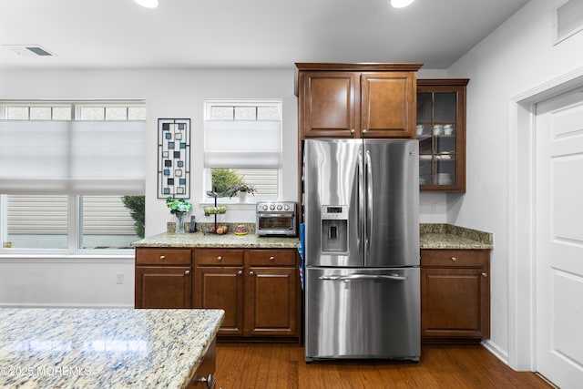 kitchen with visible vents, glass insert cabinets, light stone counters, dark wood-type flooring, and stainless steel refrigerator with ice dispenser