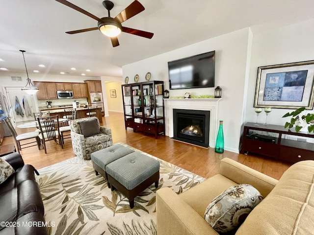 living room featuring baseboards, a ceiling fan, a fireplace with flush hearth, light wood-type flooring, and recessed lighting