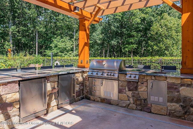 view of patio with an outdoor kitchen, area for grilling, a sink, fence, and a pergola