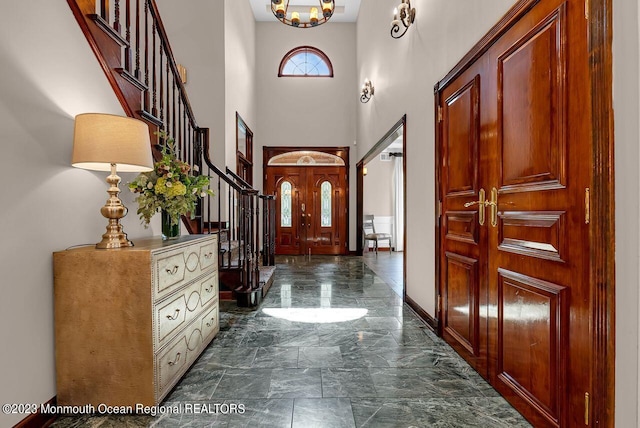 foyer entrance featuring baseboards, stone finish floor, an inviting chandelier, stairs, and a high ceiling