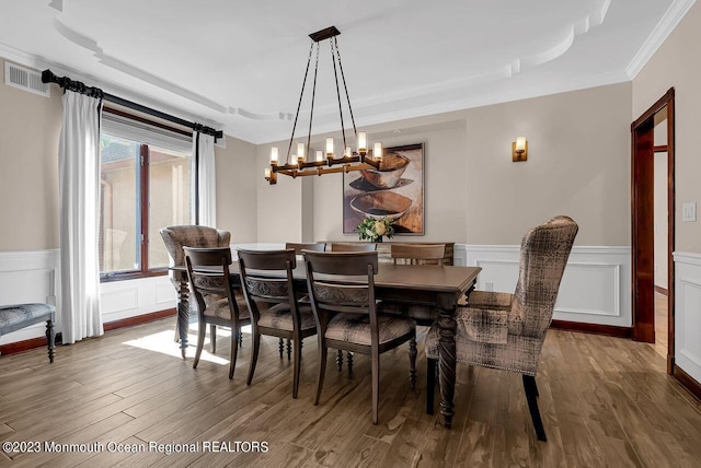 dining room featuring ornamental molding, wainscoting, visible vents, and wood finished floors