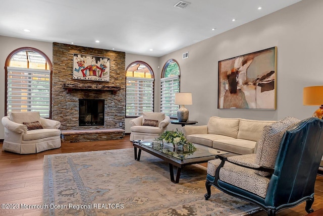 living area featuring recessed lighting, visible vents, a stone fireplace, and wood finished floors