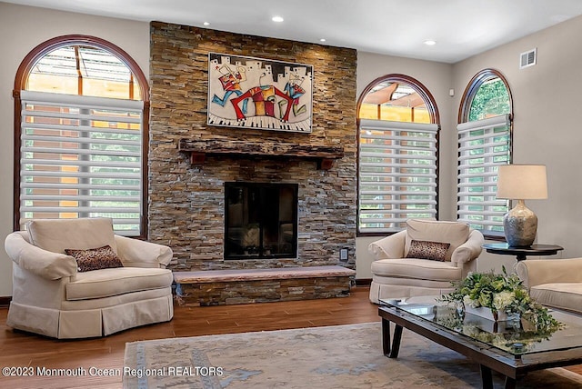 living area featuring a stone fireplace, a wealth of natural light, wood finished floors, and visible vents