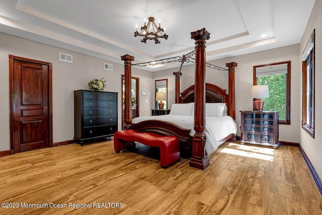 bedroom featuring a tray ceiling, light wood-style flooring, visible vents, and baseboards