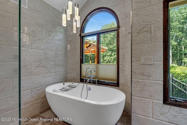 full bath with a freestanding bath, tile walls, and an inviting chandelier