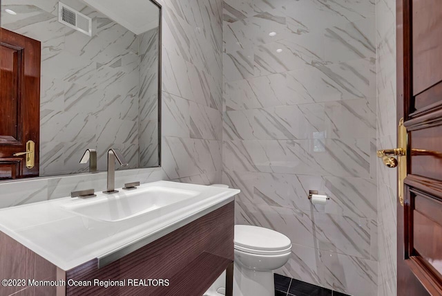 half bathroom with toilet, visible vents, tile walls, and vanity