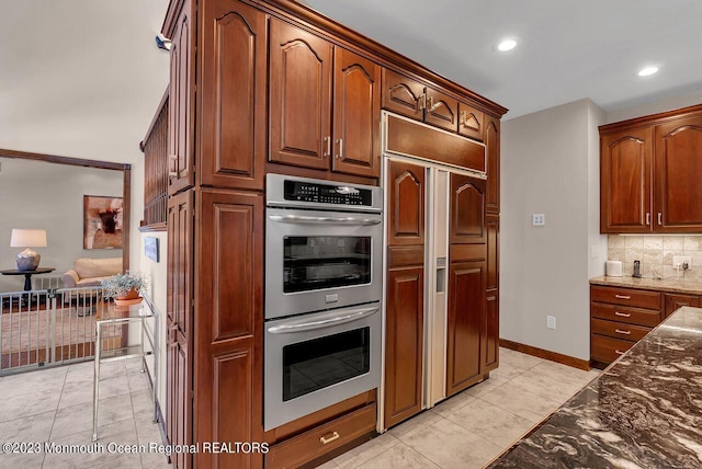 kitchen featuring stainless steel double oven, light tile patterned flooring, paneled refrigerator, backsplash, and dark stone countertops