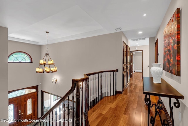 hallway with visible vents, wood finished floors, an upstairs landing, and an inviting chandelier