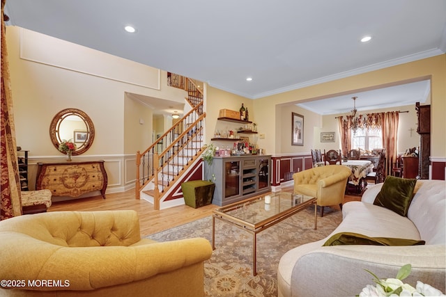 living area with wainscoting, stairway, wood finished floors, crown molding, and a decorative wall