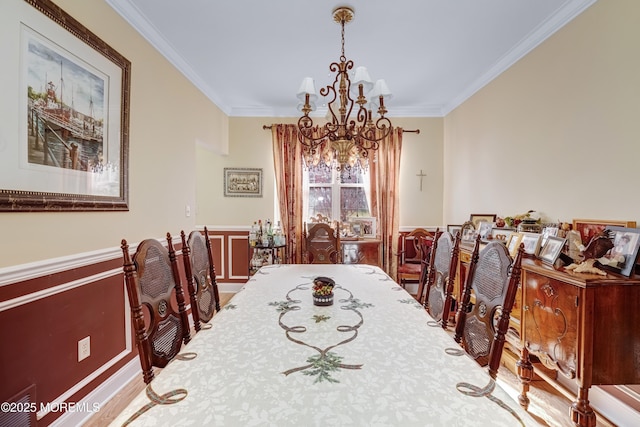 dining room with a chandelier, ornamental molding, a wainscoted wall, and wood finished floors