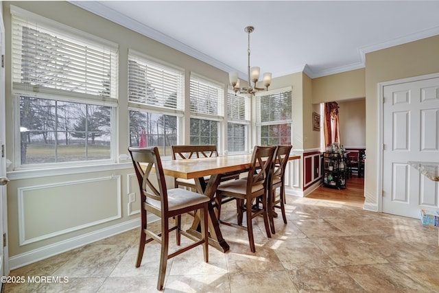 dining room with a chandelier, ornamental molding, wainscoting, and a decorative wall