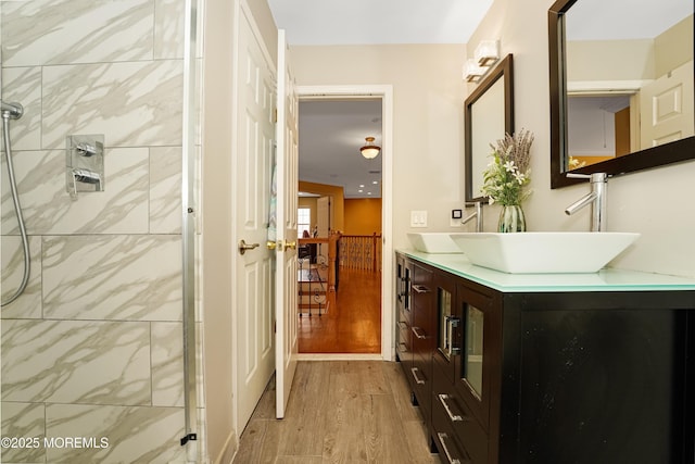 full bath featuring a sink, double vanity, tiled shower, and wood finished floors