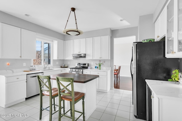 kitchen with tasteful backsplash, appliances with stainless steel finishes, light tile patterned flooring, a kitchen island, and under cabinet range hood