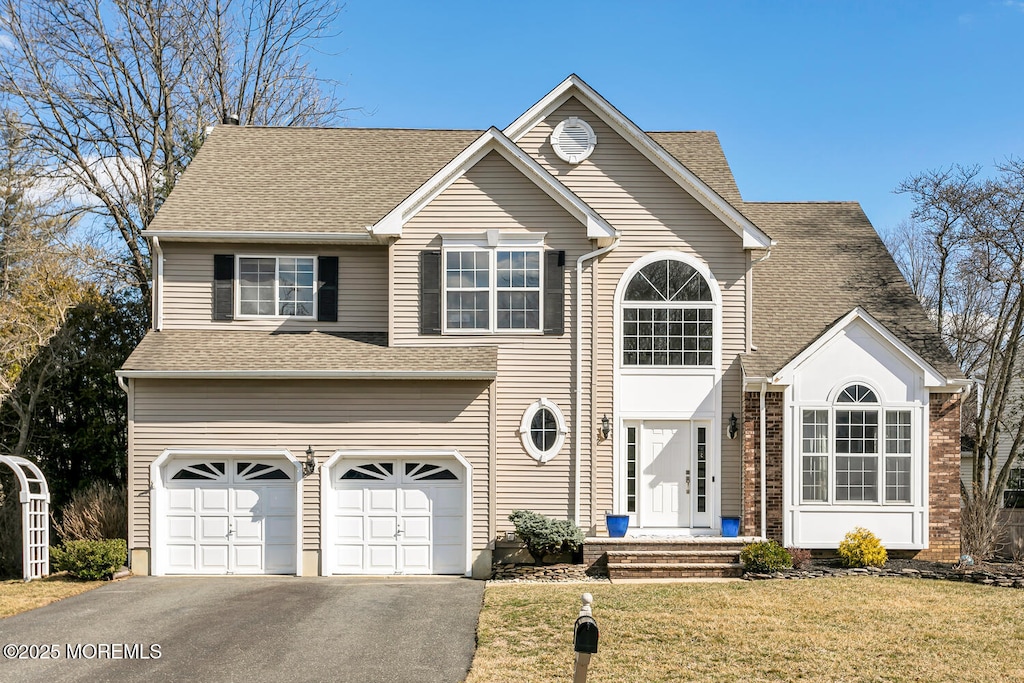 traditional-style home featuring an attached garage, driveway, a front lawn, and roof with shingles